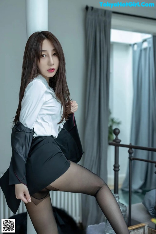 A woman in a white shirt and black skirt posing on a bed.