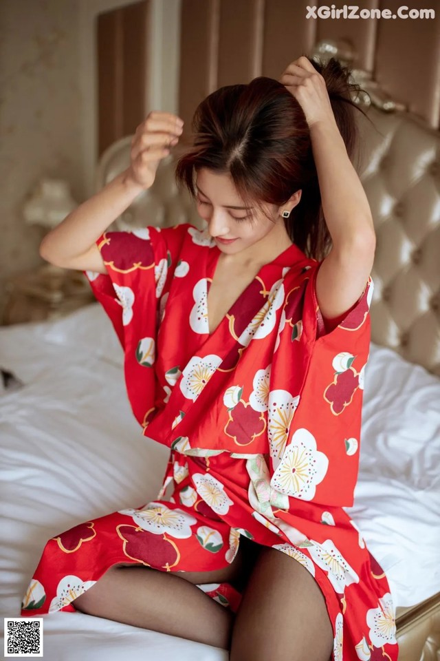 A woman in a red kimono sitting on a bed.