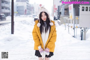 A woman in a yellow jacket is walking in the snow.