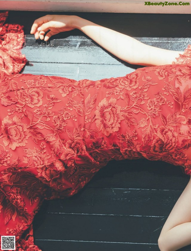 A woman in a red dress laying on a wooden floor.