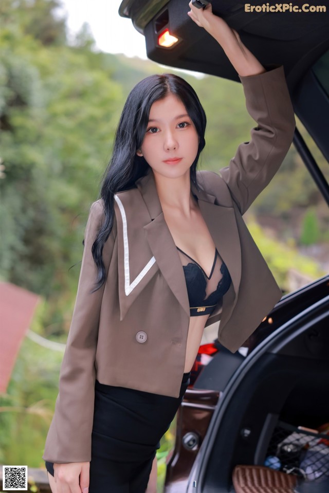 A woman in a brown blazer and black skirt standing next to a car.