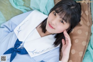 A woman in a school uniform sitting on a bed.