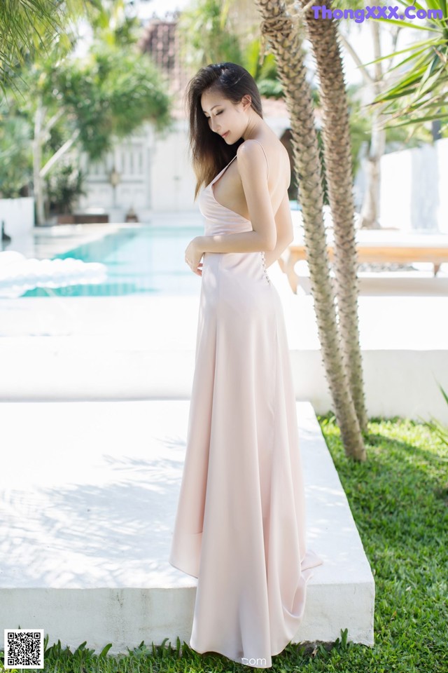 A woman in a pink dress standing next to a pool.