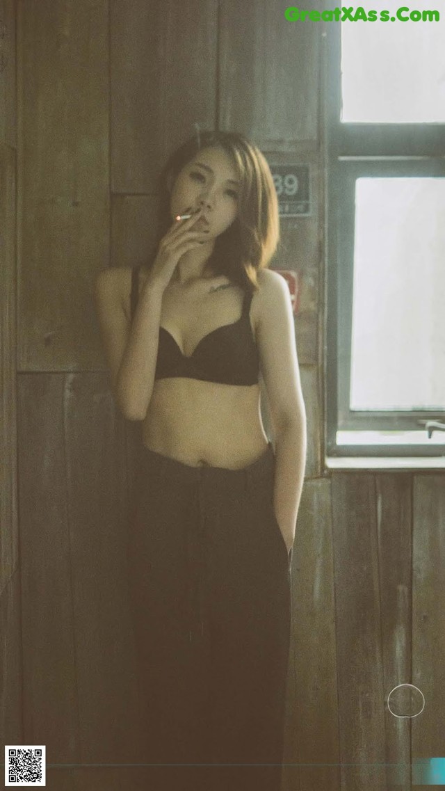 A woman in a black bra top smoking a cigarette.