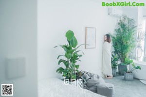 A naked woman standing next to a plant in a room.