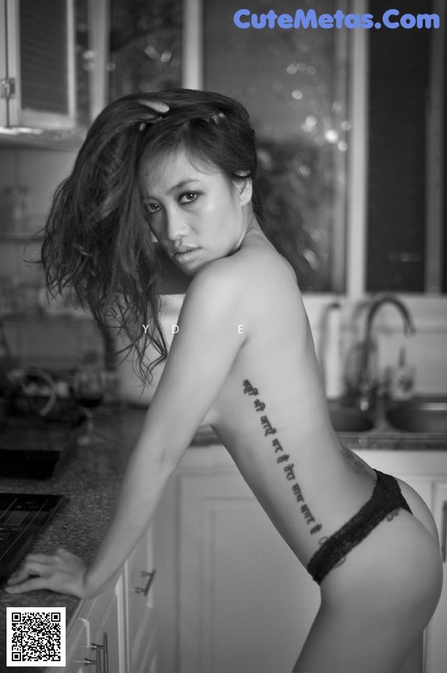 A woman with a tattoo on her back standing in a kitchen.