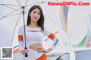 A woman in a white and orange outfit holding an umbrella.