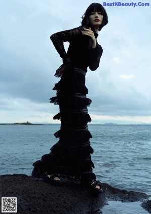 A woman in a black dress sitting on a chair.