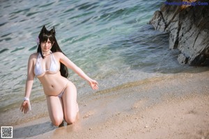 A woman in a white bikini sitting on a rock by the water.