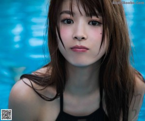 A woman in a white bikini leaning against a pink wall.